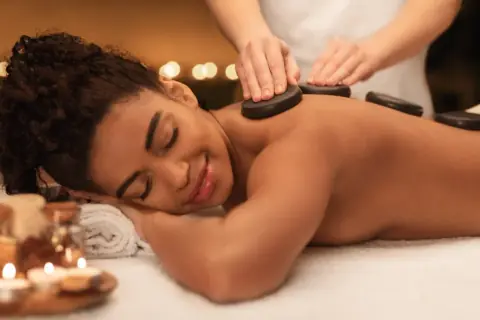 Client lying face down receiving a hot stone massage along the spine