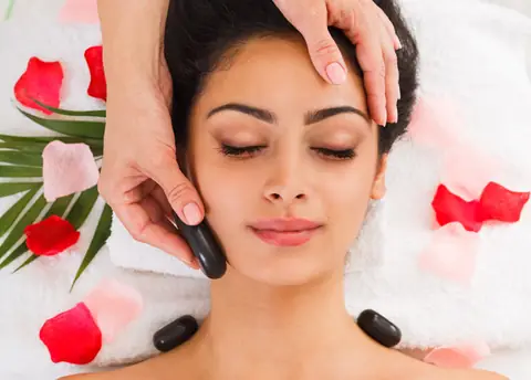 Stone massage being placed along a woman’s back at a spa